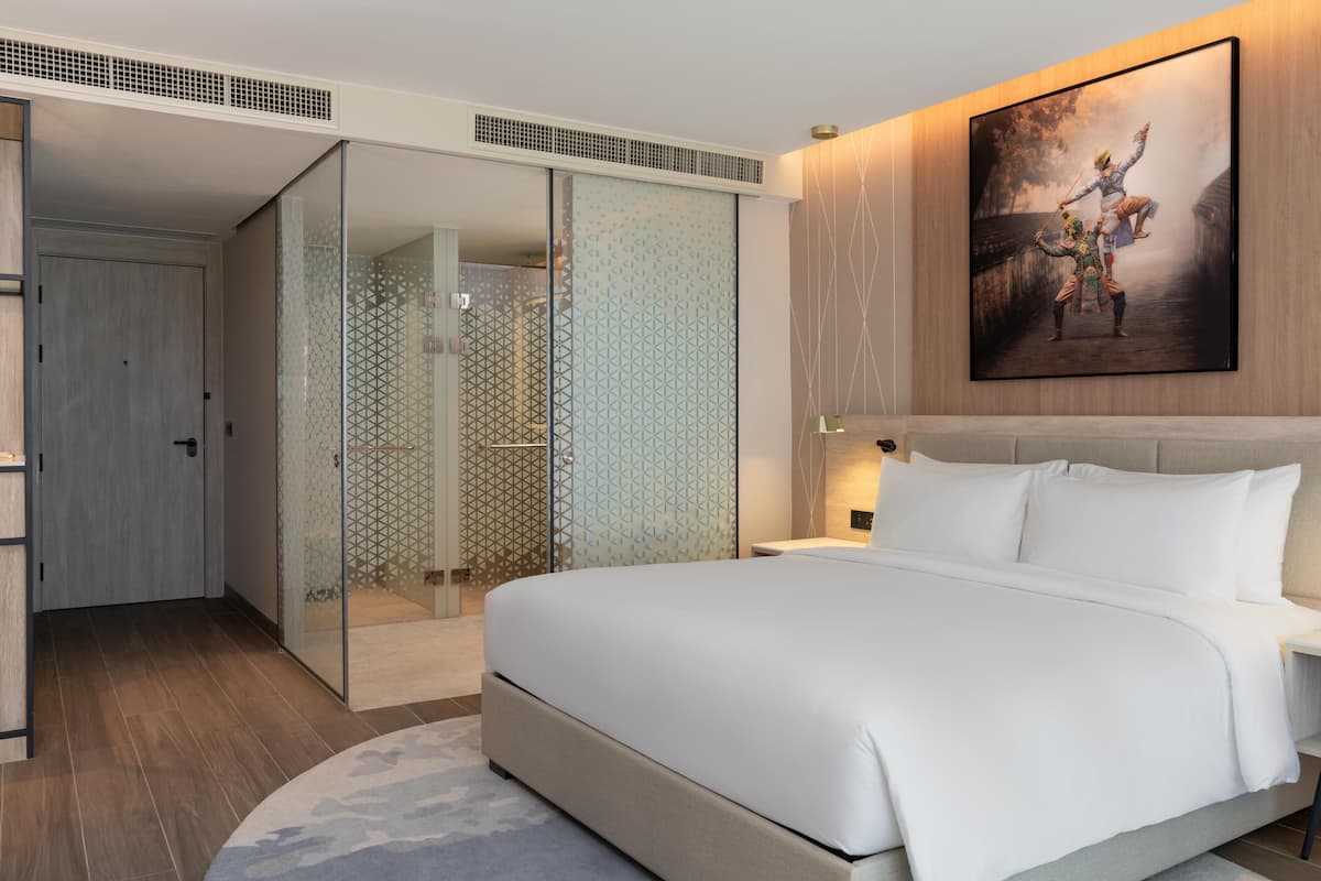 Una habitación de hotel moderna con una cama grande, ducha envuelta en vidrio y un cuadro en la pared.