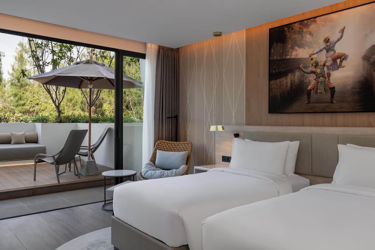 Habitación de hotel moderna con una cama grande, un sofá, una silla, una mesita y un balcón con sombrilla.