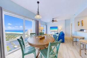 A spacious room with a large dining table, chairs, a ceiling fan, and a view of the ocean. - 16th-Floor Gulf Views | Luau 7609 | Optional Studio Add-On NEW Listing (Miramar Beach)