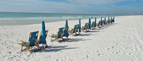 En strand med rækker af blå strandstole og parasoller langs kystlinjen.