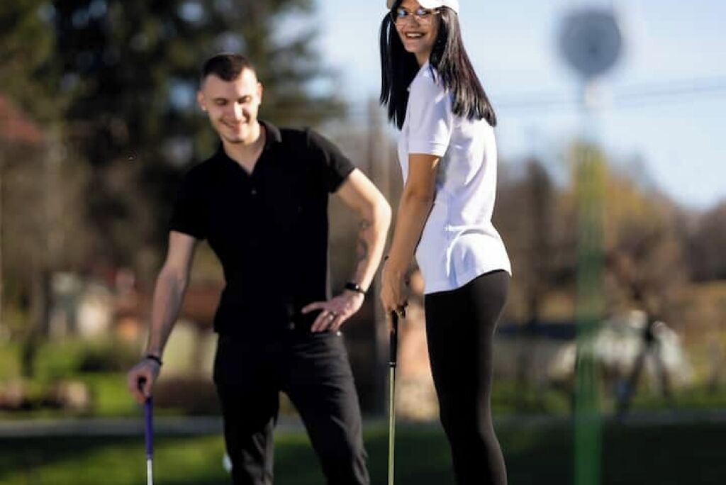 Deux personnes se promènent sur un terrain de golf, avec un ciel dégagé et des arbres en arrière-plan.
