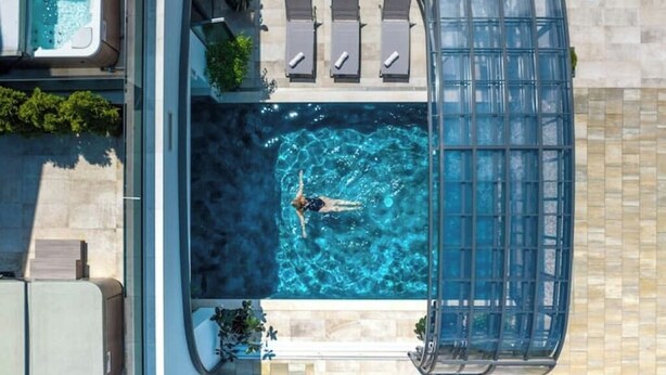 Ein Luftbild eines Poolbereichs auf einem Dach mit einer Person, die schwimmt, Liegestühlen und einer Whirlwanne.