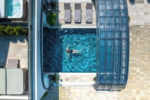 Vue aérienne d’un espace piscine sur le toit, où l’on aperçoit une personne nageant, des chaises longues et un jacuzzi.