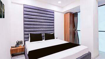A modern hotel room with a large bed, a wooden nightstand, a headboard with a textured design, and a view of the outdoors through a window.