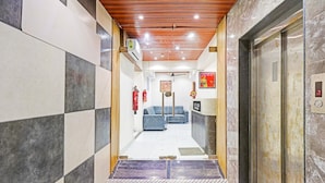 A hotel lobby with a checkered floor pattern, a reception desk, a blue sofa, and an elevator. - Classic Hotel Niraant (Surat)