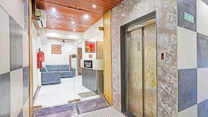 A hotel lobby with a reception desk, a blue sofa, an elevator, and a fire extinguisher. - Classic Hotel Niraant (Surat)