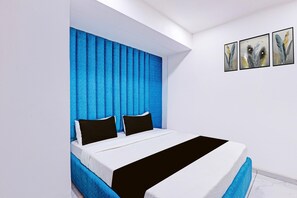 A modern bedroom with a blue headboard, a large bed with white and black bedding, and three framed artworks on the wall. - Classic Hotel Niraant (Surat)