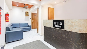 A hotel reception area with a reception desk, a blue sofa, a wooden ceiling, and a fire extinguisher. - Classic Hotel Niraant (Surat)