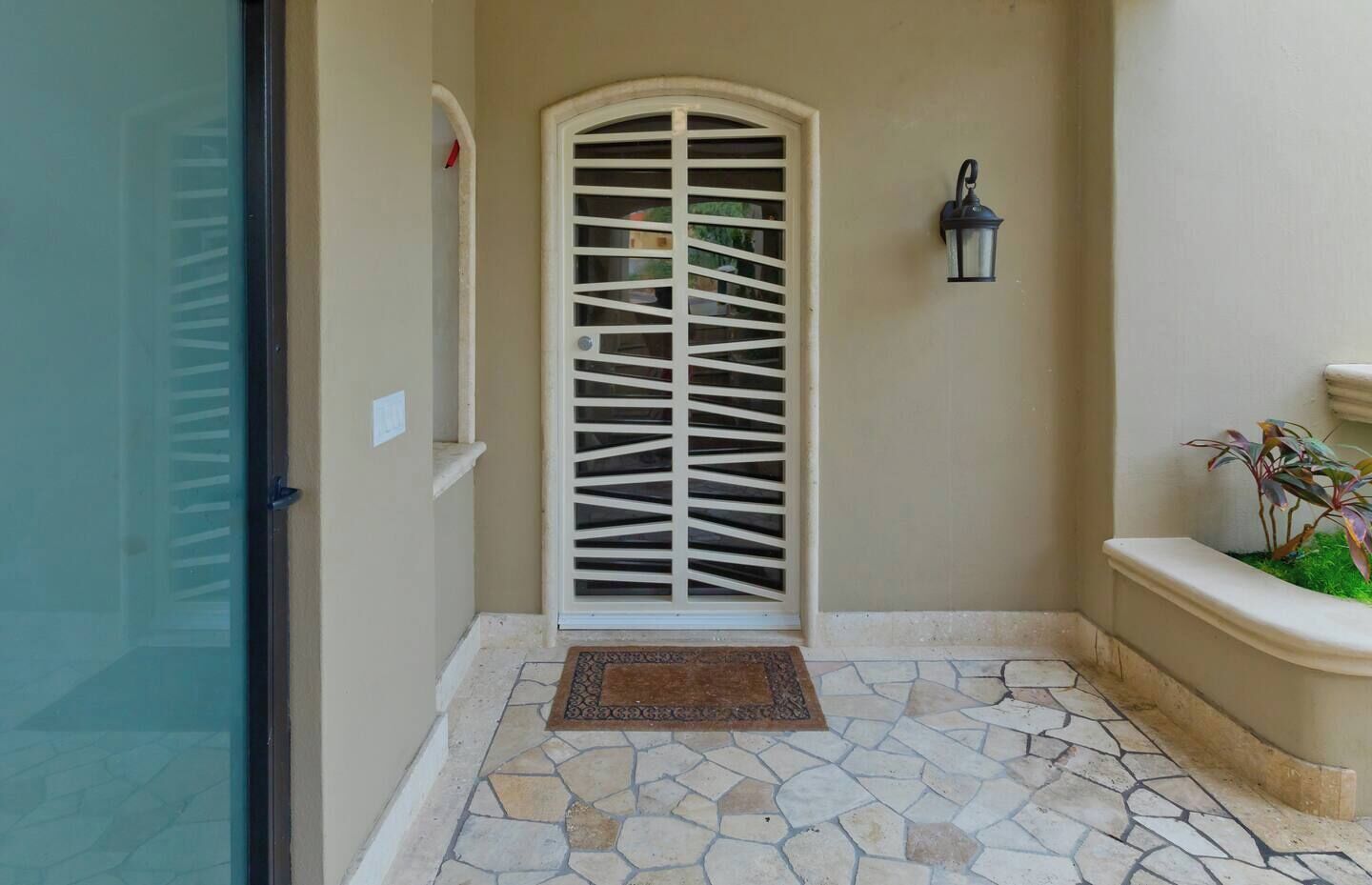 A stone-tiled entrance with a white decorative door and a small planter with plants.