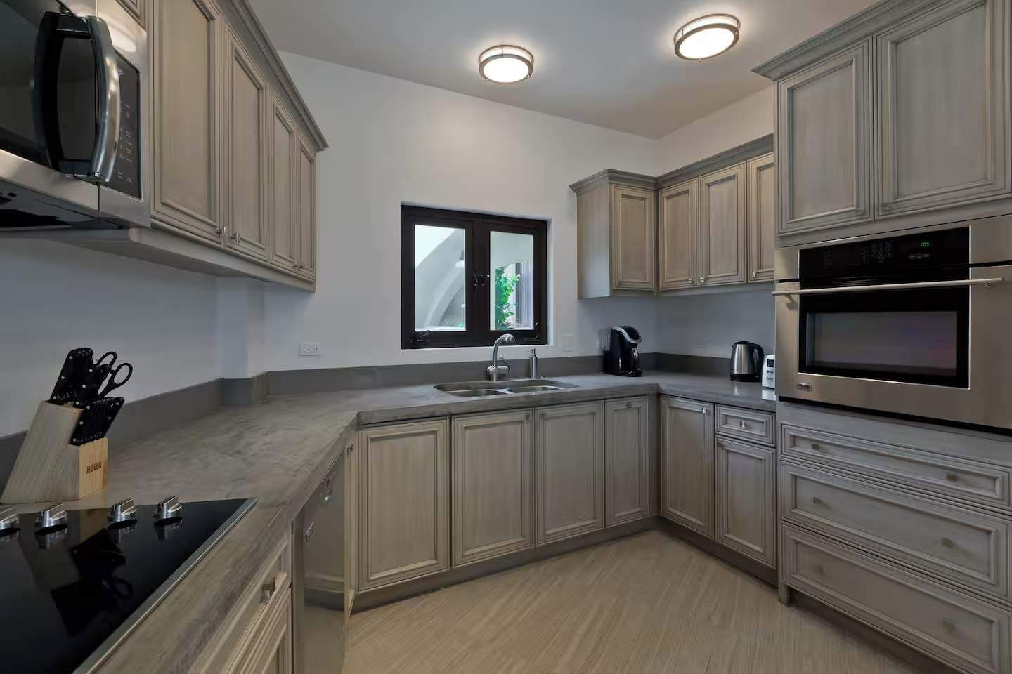 A modern kitchen with built-in appliances, a window, and a view of greenery outside.