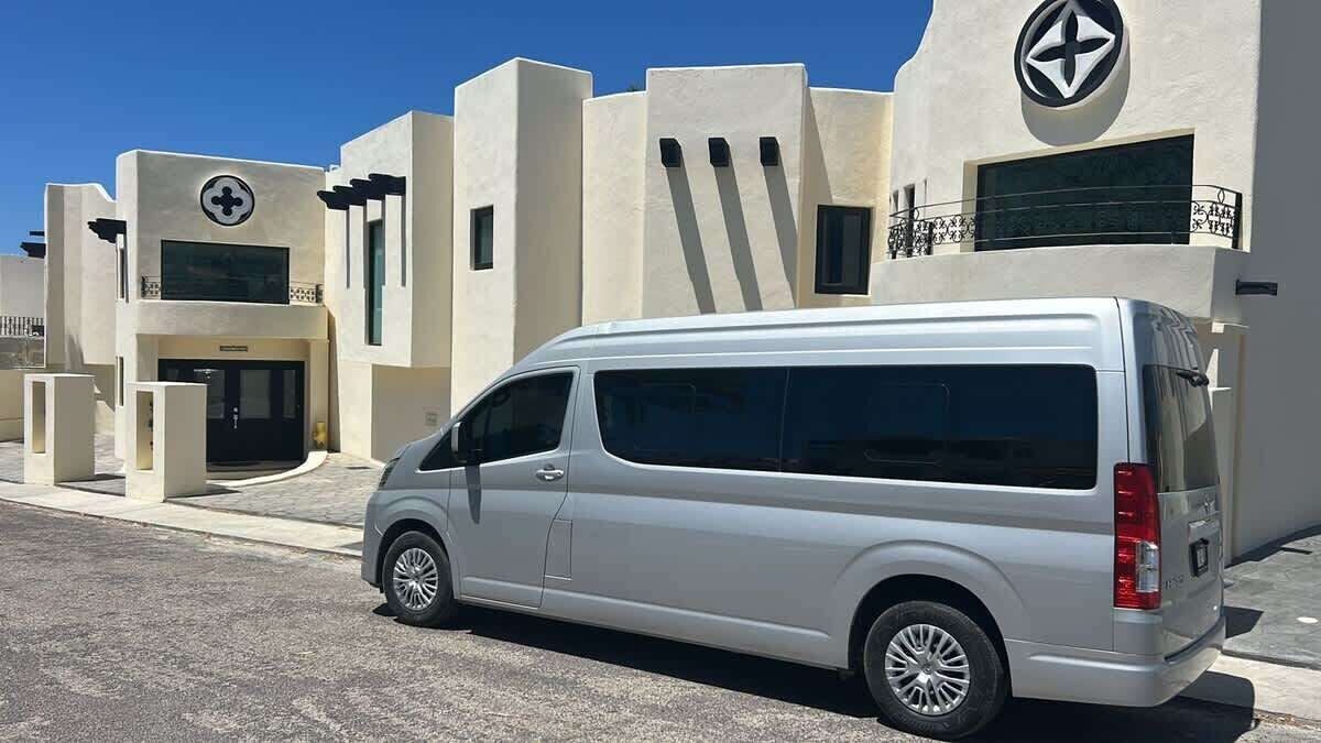 A silver van parked in front of a building with a modern design, featuring a circular logo and a balcony with a railing.