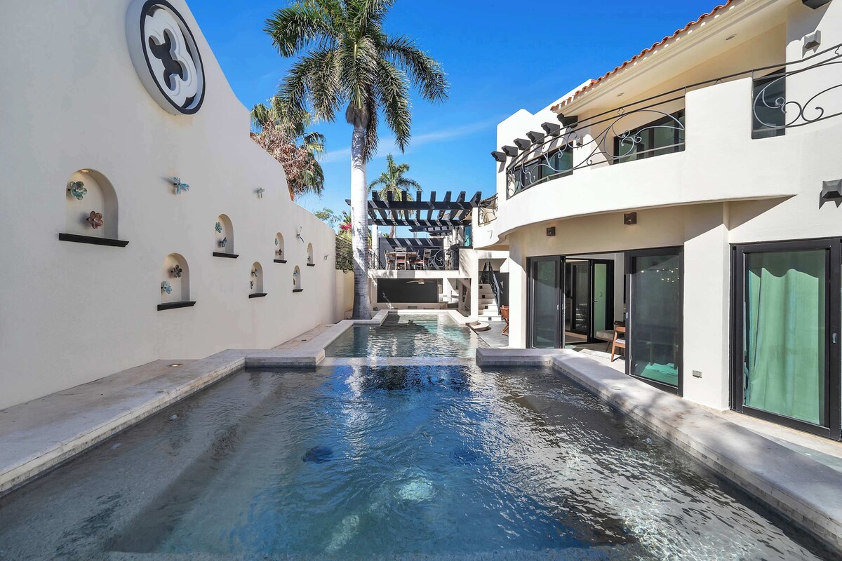 A swimming pool with a pergola, palm trees, and a modern building with balconies.