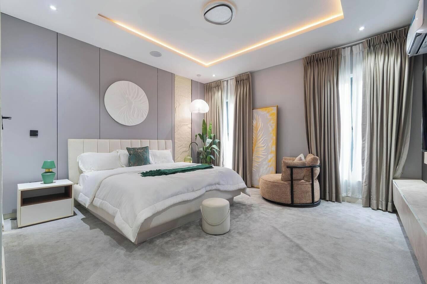 Ein modernes Schlafzimmer mit einem großen Bett, Nachttischen, einem runden Sessel und einem großen Fenster mit Vorhängen.