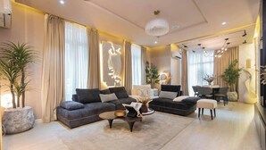 A modern living room with a sectional sofa, a round coffee table, and a dining area with a unique curved chair. - Phaluxe Shortlets (Abuja)