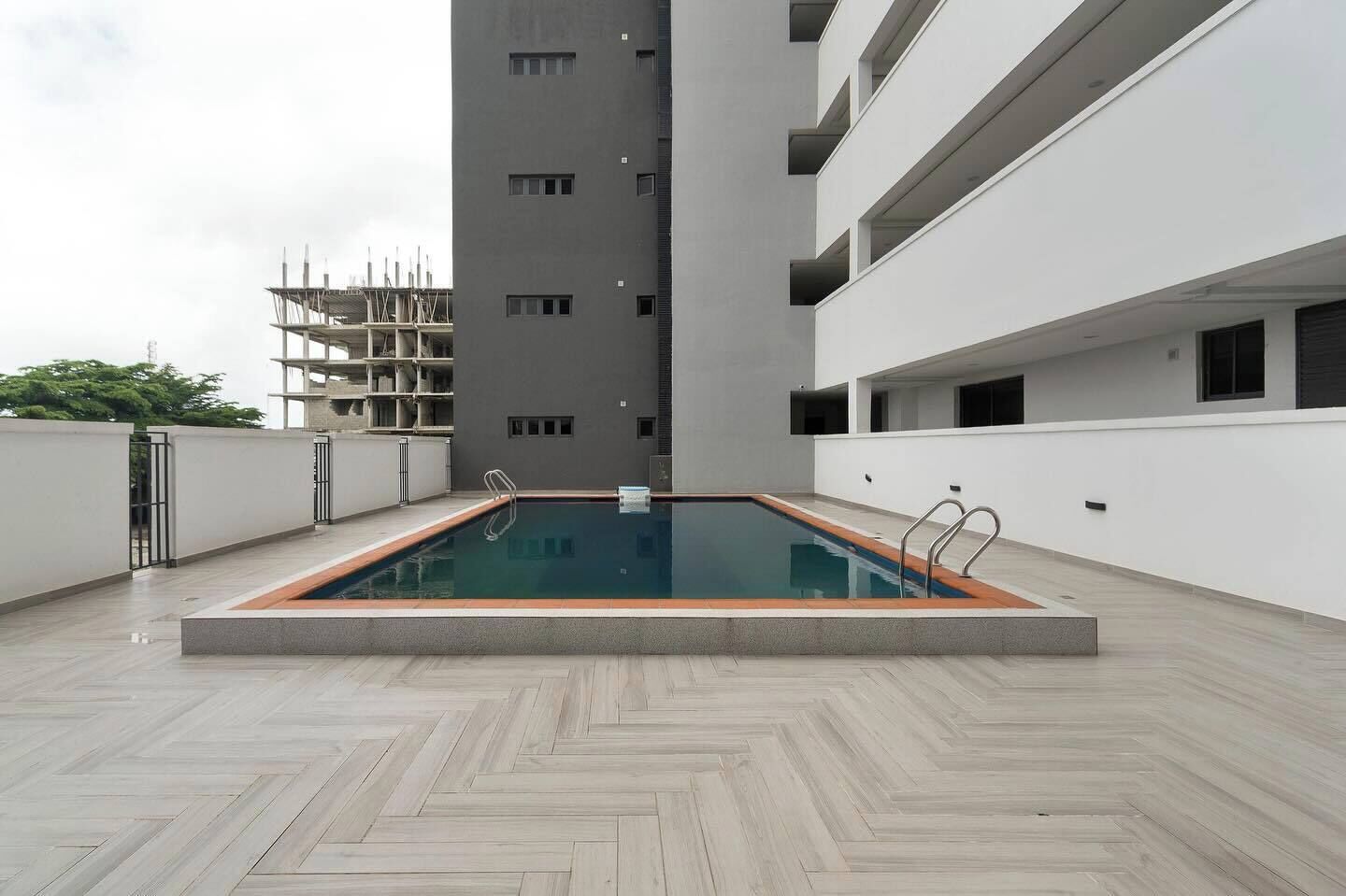 Ein Dachpool mit Fischgrätmuster-Fliesen, umgeben von einem weißen Gebäude mit mehreren Balkonen.