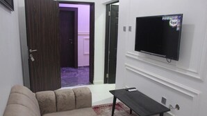A living room with a beige sofa, a small black table, and a mounted TV on the wall. - ZYNA VILLE (Abuja)