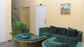 A living area with a green sofa and matching ottoman, a staircase with a railing, and a door with a number sign. - ZYNA VILLE (Abuja)