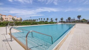 Ein Schwimmbecken mit Metallgeländern, umgeben von einer gepflasterten Terrasse und Palmen.