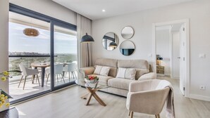 Ein modernes Wohnzimmer mit einer Couch, Sesseln, einem Glastisch und Blick durch große Fenster.