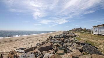 Ein Strand mit felsigem Ufer, blauem Himmel und einem Gebäude in der Ferne.