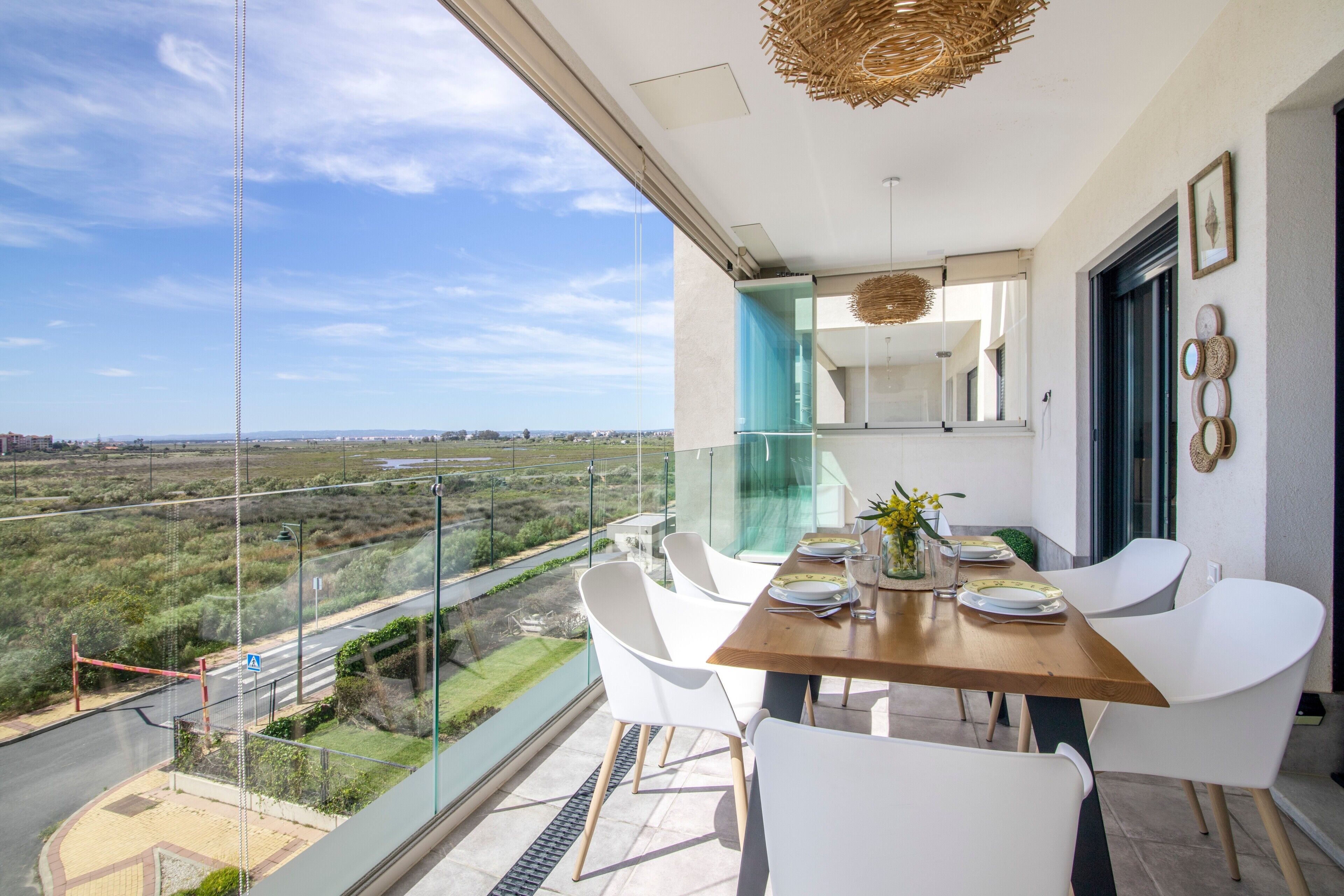 A balcony with a dining table, white chairs, and a view of the countryside.