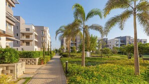 A pathway lined with palm trees and greenery, leading to modern apartment buildings with balconies. - Luxury 3BR Serviced Apartment At Aeon Tower (6th of October City)