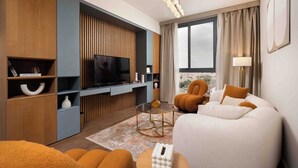 A modern hotel room with a large TV, comfortable seating, a city view, and a stylish decor. - Luxury 3BR Serviced Apartment At Aeon Tower (6th of October City)
