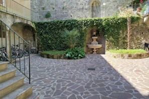 Een binnenplaats met stenen vloer, een fontein en een trap naar een hoger gelegen niveau.