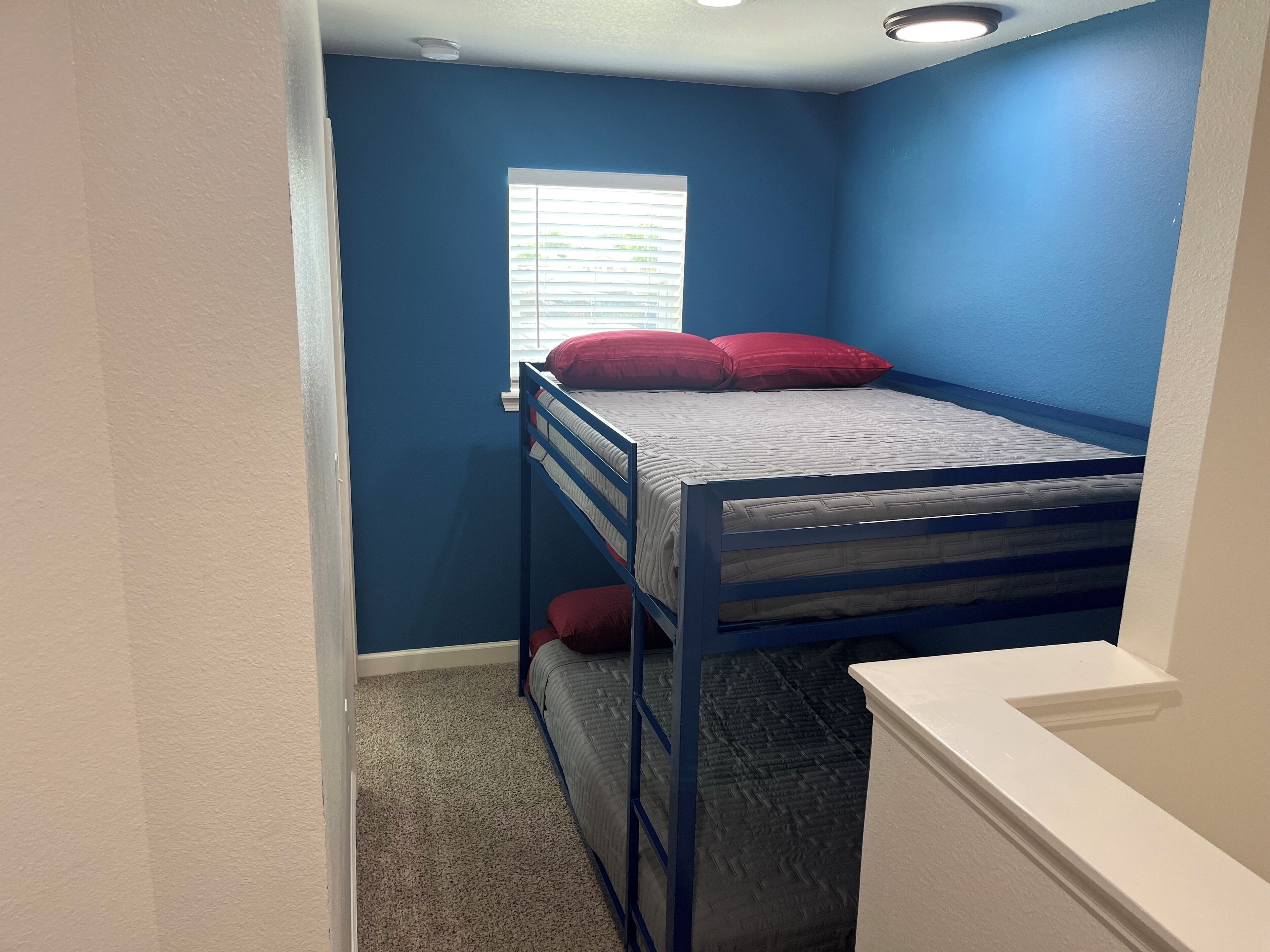 A bunk bed with red pillows in a room with blue walls and a window with blinds.
