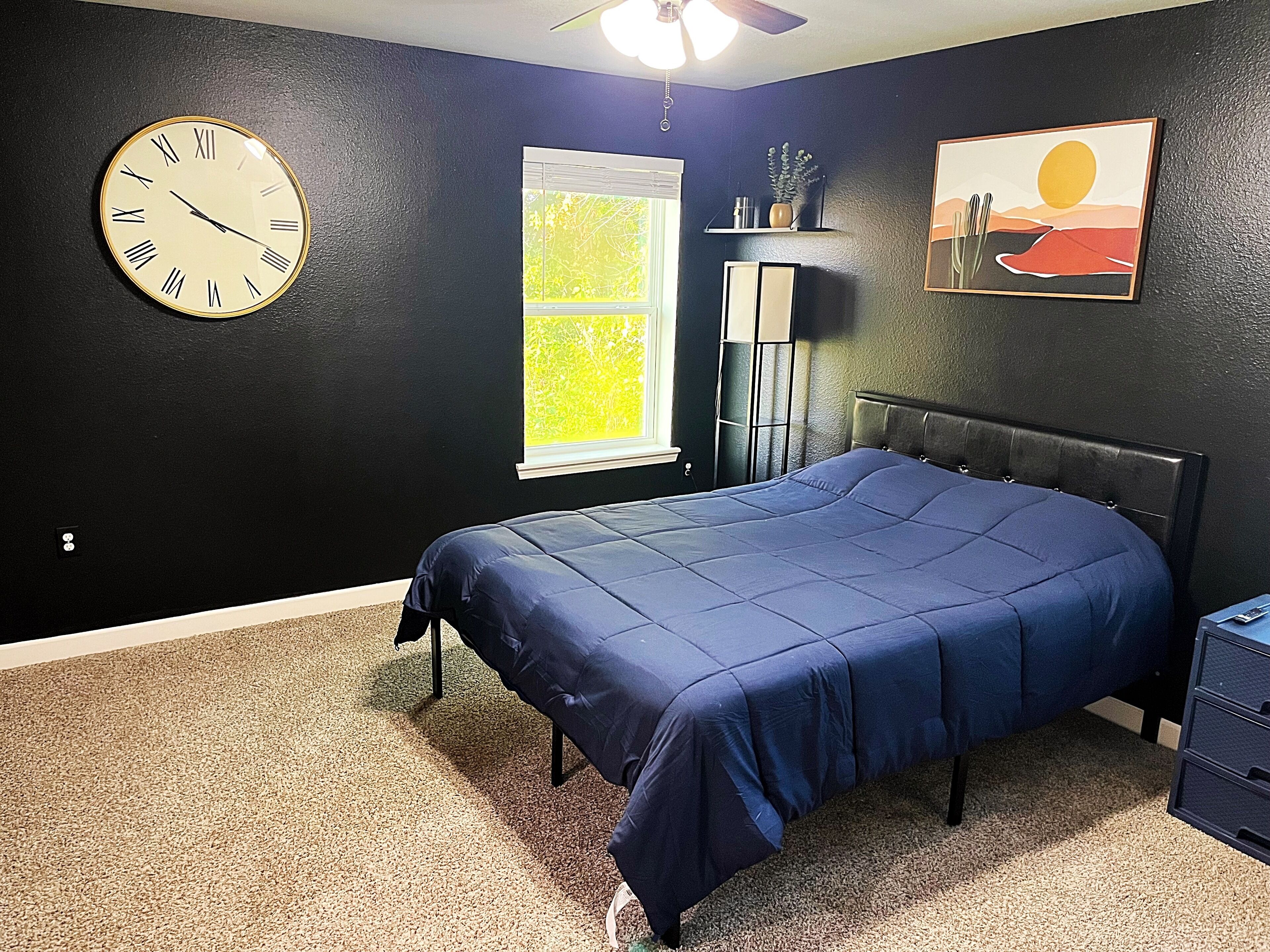 A bedroom with a bed, a wall clock, a window, and a painting.
