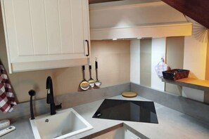 A kitchen with a white sink, black faucet, and a black induction cooktop. There are utensils hanging on the wall and a basket on the countertop. - CasaFedra:Elegant Loft on the lakefront in the Heart of the Historic Center (Toscolano Maderno)