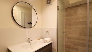 A modern bathroom with a round mirror, a white sink, a towel, and a glass shower enclosure. - w Amazing Loft w Balcony in Miraflores (Lima)