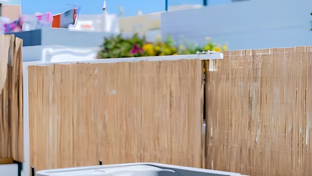 Un moderno jacuzzi al aire libre con escalones, frente a una valla de madera y un cielo azul despejado.