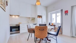 Una cocina moderna con armarios blancos, horno empotrado y comedor con mesa y sillas.