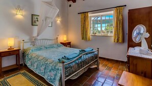 Una camera da letto con un letto, lampade da comodino, una finestra con tende, un comodino, una ventola e un soffitto in legno.