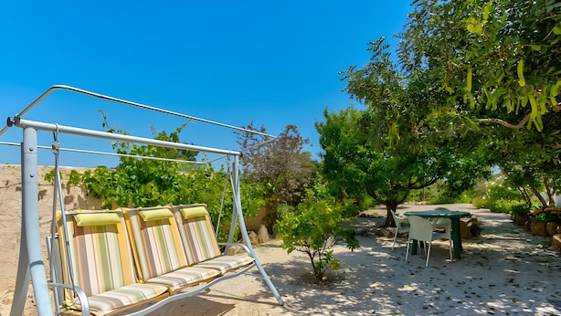 Un'area patio con altalena, tavolo e sedie, e un piccolo albero.