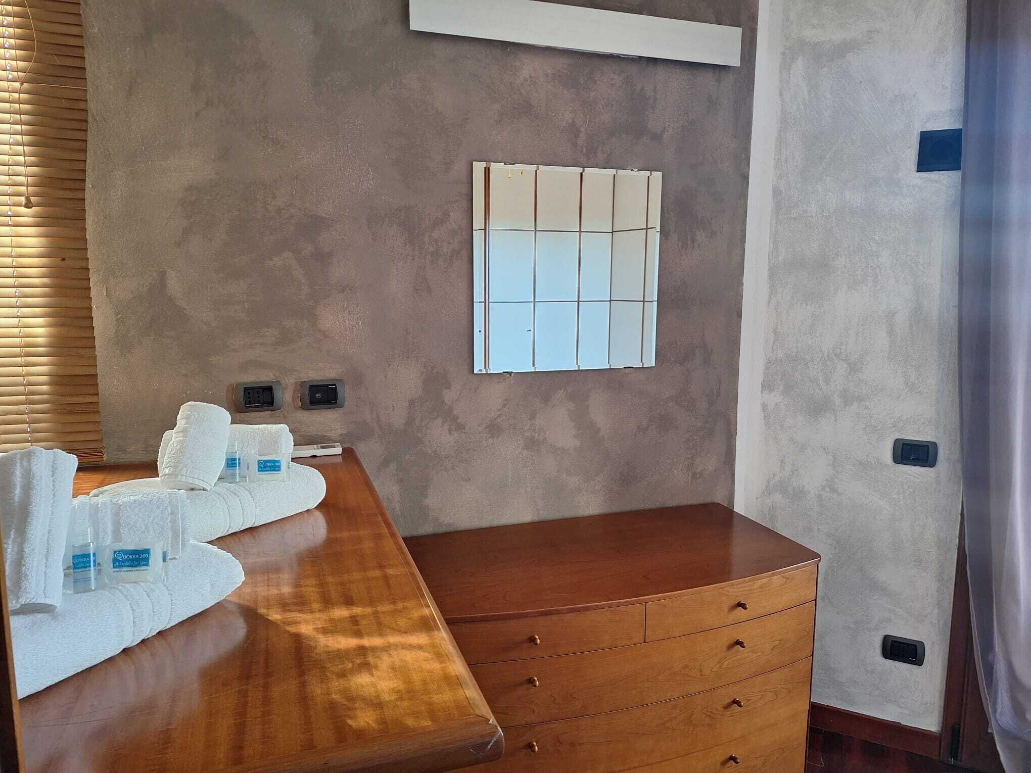 A hotel room with a wooden dresser, a large window with blinds, and a wall-mounted control panel.