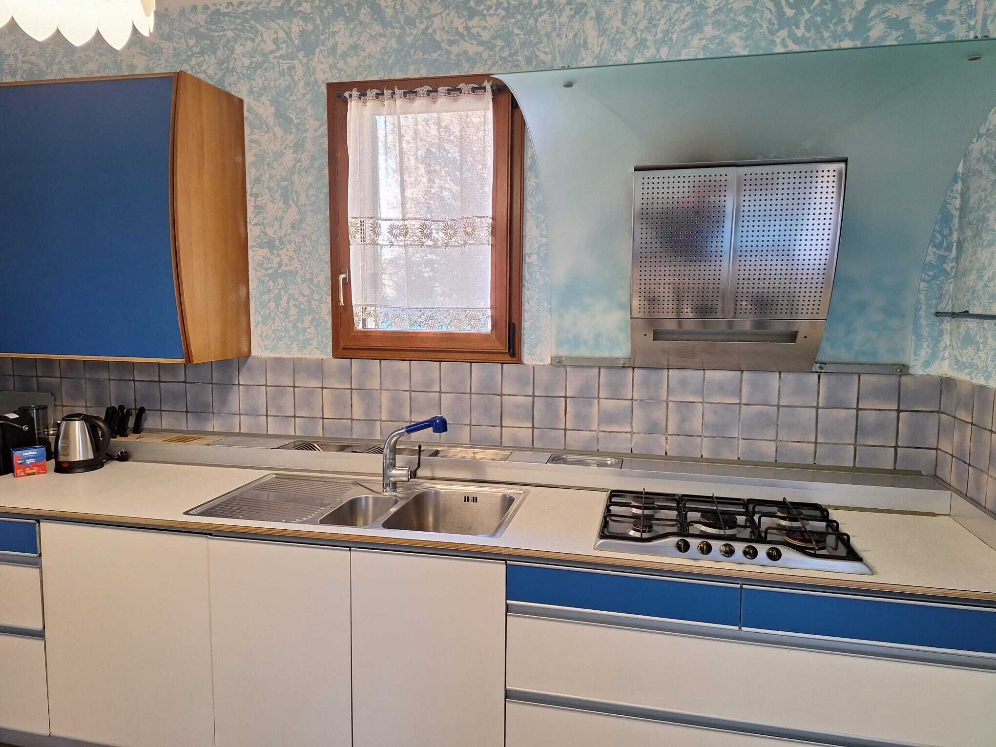 Une cuisine équipée d’un évier, d’une cuisinière et d’une fenêtre ornée de rideaux en dentelle.