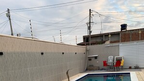 A rectangular swimming pool with a tiled edge, surrounded by a concrete deck. There are chairs and a table in the background. - Modern house in Zé Pojuca / Porto de Galinhas (Ipojuca)