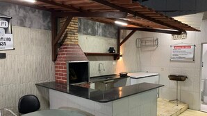 A kitchen with a brick oven, a sink, and a countertop. There is a sign on the wall and a table with chairs. - Modern house in Zé Pojuca / Porto de Galinhas (Ipojuca)