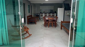 A dining area with a wooden table and chairs, a kitchen in the background, and a glass partition on one side. - Modern house in Zé Pojuca / Porto de Galinhas (Ipojuca)
