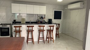 A kitchen with white cabinets, a stove, and four wooden bar stools. - Modern house in Zé Pojuca / Porto de Galinhas (Ipojuca)