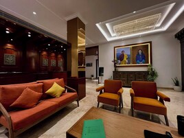 A lobby with a red sofa, two orange armchairs, a wooden coffee table, and a ceiling light fixture.