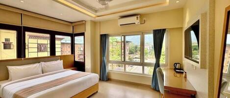Une chambre d’hôtel avec un lit, une télévision, un ventilateur de plafond et une fenêtre avec des rideaux.