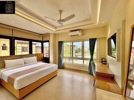 A hotel room with a bed, a TV, a ceiling fan, and a window with curtains.