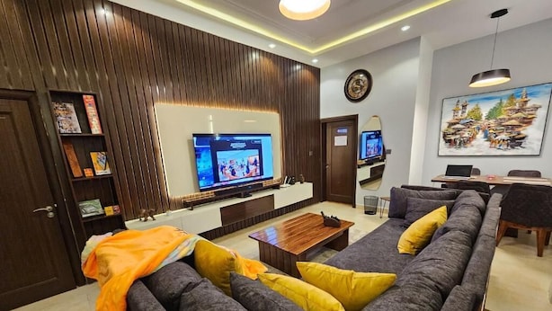 A modern living room with a large sectional sofa, a flat-screen TV, and a dining area with a laptop on the table. - Meros Villa Apartment (Lagos)
