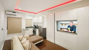 A modern living room with a sofa, a television, and a kitchen area with appliances. - Meros Villa Apartment (Lagos)