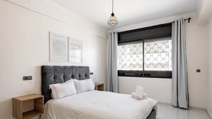 Une chambre à coucher moderne avec un grand lit, une table de chevet, une commode et une fenêtre avec des rideaux.