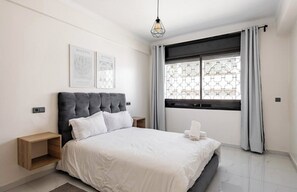 A modern bedroom with a large bed, a bedside table, a nightstand, and a window with curtains. - Modern & Central 2 bedroom at Rabat Hassan City Center / 3min train station (Rabat)