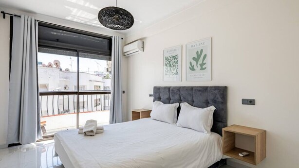 Une chambre à coucher moderne avec un grand lit, une tête de lit rembourrée de couleur grise et deux tables de chevet.